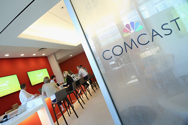 Several people are seated at a long table. A sign in front indicates that this is a Comcast office.