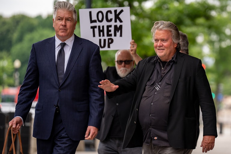 Steve Bannon and his lawyer walk in front of a man holding a "Lock Them Up" sign.