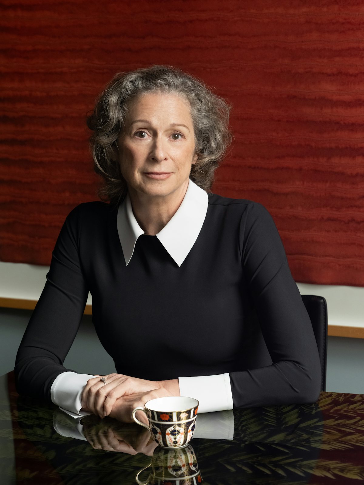Heiress Abigail Disney, dressed elegantly in black, photographed sitting in front of a red contemporary art work at her dining room table in her home in New York City.