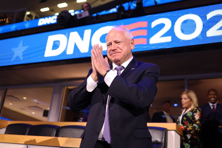 Tim Walz puts his hands together as if in prayer. A large sign behind him reads DNC 2024.