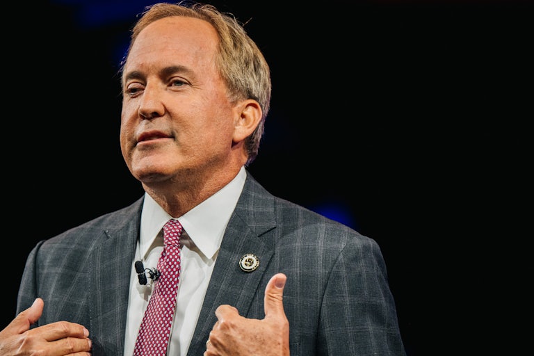 Ken Paxton points towards himself while wearing a plaid suit