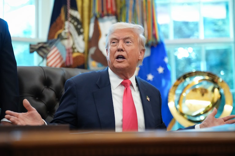 Donald Trump holds his hands out to the side and speaks while sitting at his desk in the Oval Office.