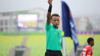 Omar Artan holds up a yellow card while refereeing a match.