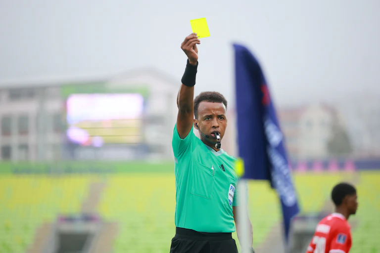 Omar Artan holds up a yellow card while refereeing a match.