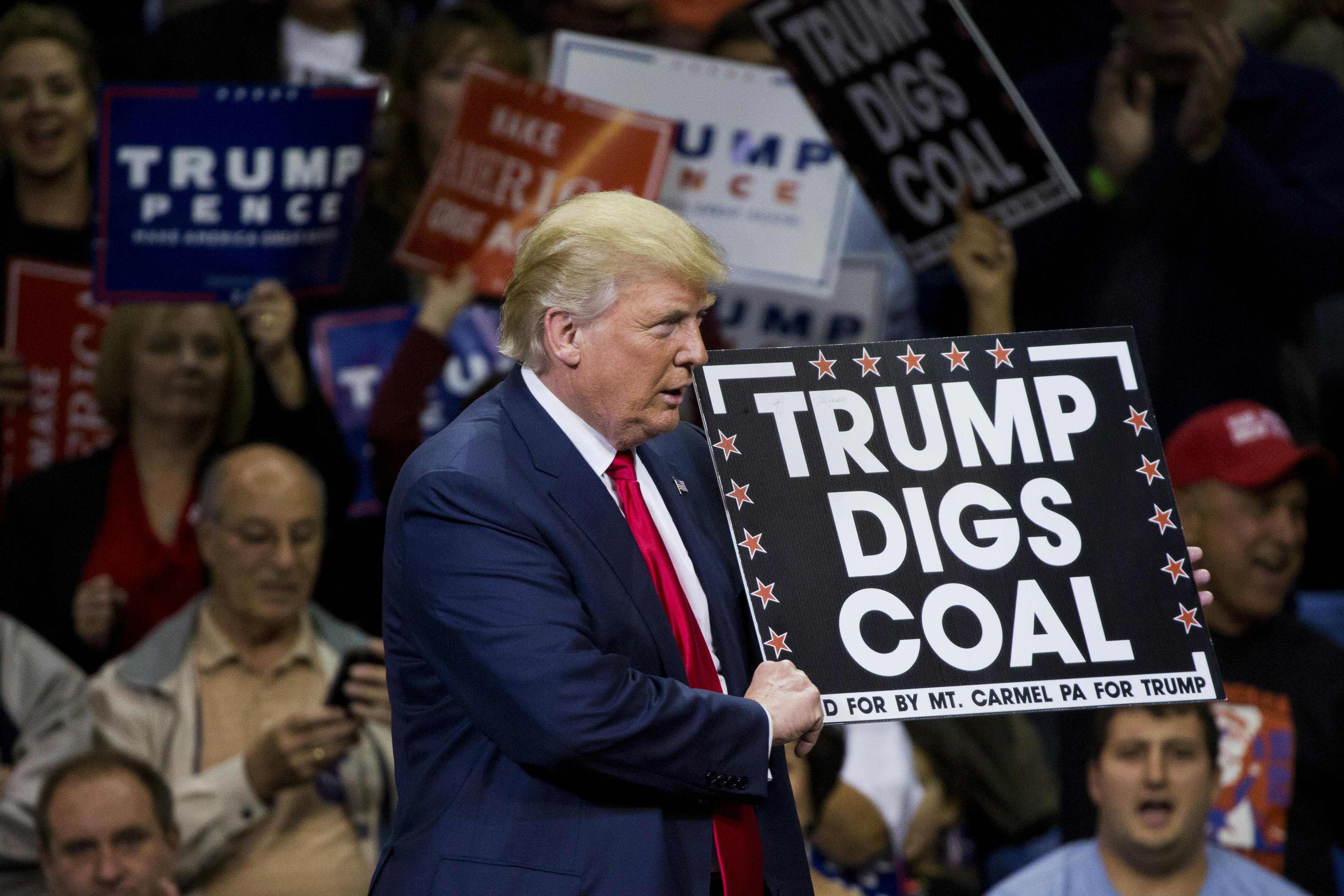 Trump holds a sign reading "Trump digs coal" in front of a crowd.