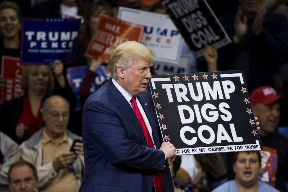 Trump holds a sign reading "Trump digs coal" in front of a crowd.