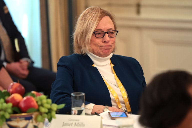 Maine Governor Janet Mills presses her lips together while sitting in the White House and listening to Donald Trump speak