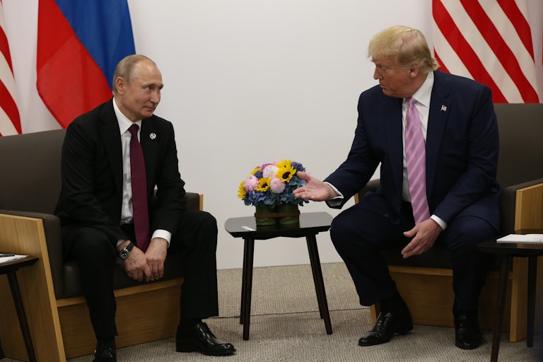 Donald Trump extends a hand as he sits on a chair across from Russian President Vladimir Putin, who looks at him with his eyebrows raised.