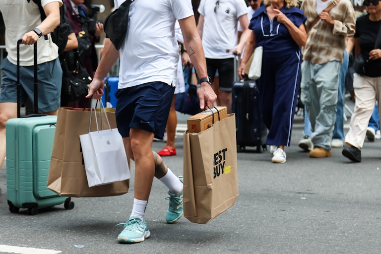 People carrying shopping bags walk down a busy street.