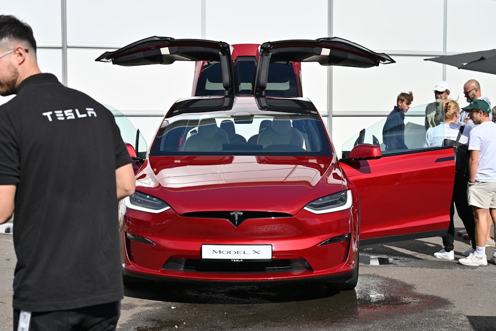 People cluster around a red Tesla Model X with its doors open.