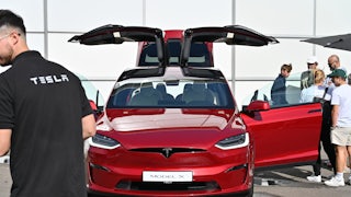 People cluster around a red Tesla Model X with its doors open.