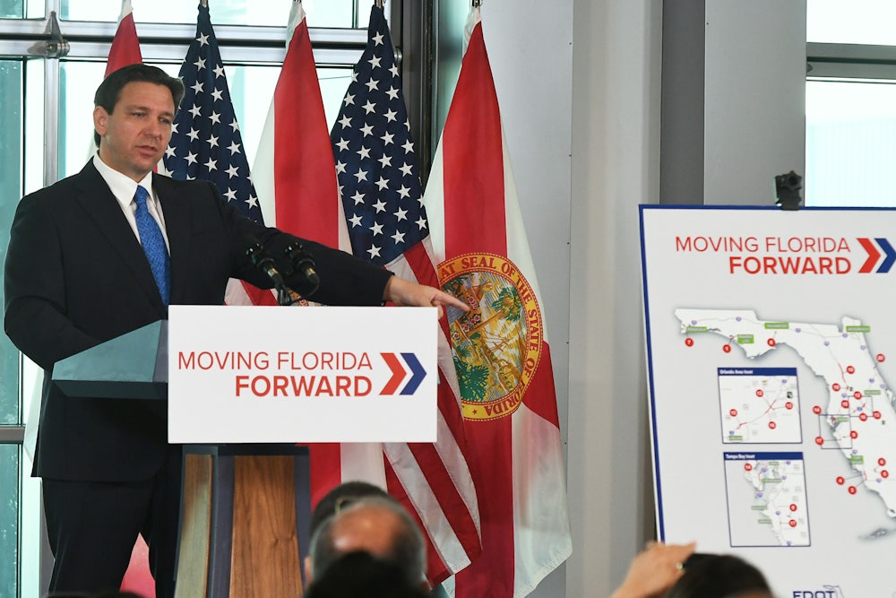 Ron DeSantis stands at a podium reading "Moving Florida Forward."