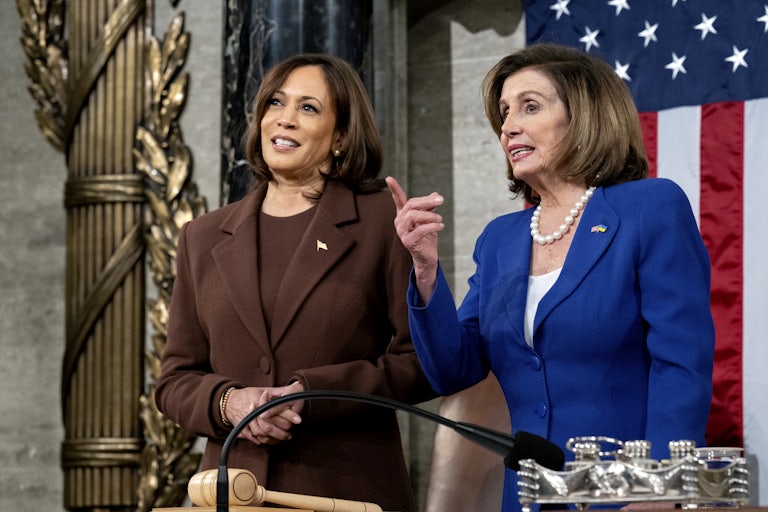 Nancy Pelosi points and Kamala Harris stands next to her smiling, hands clasped. They are in the U.S. Capitol.
