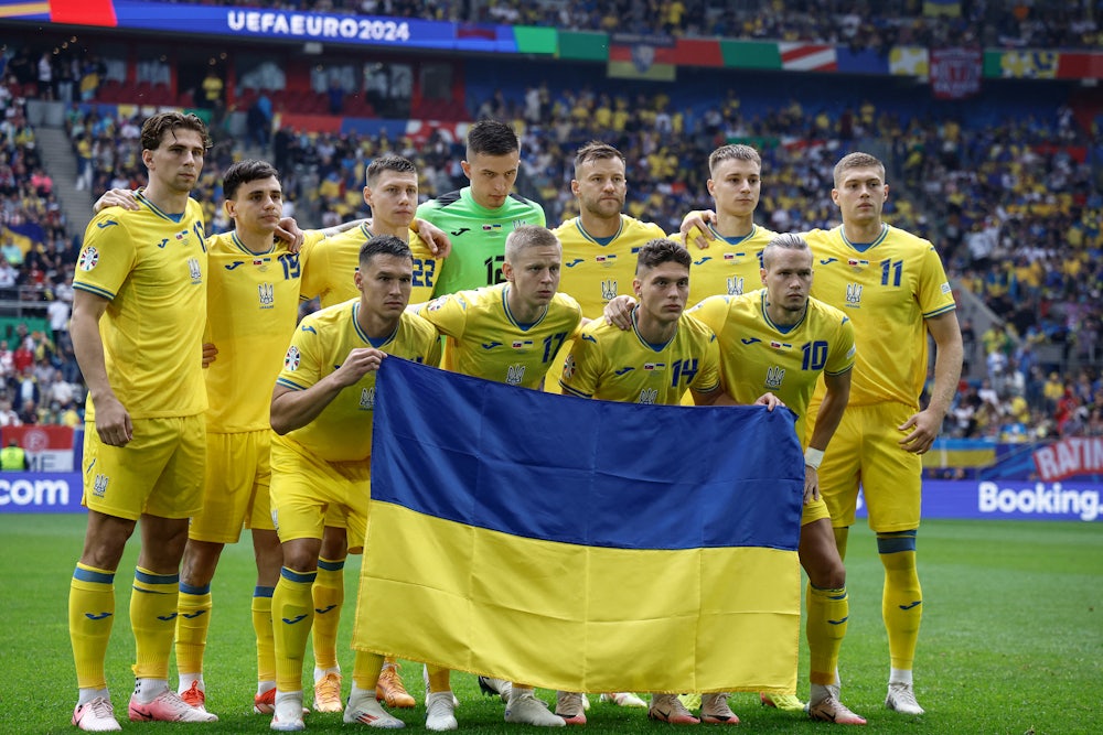 A soccer team wearing yellow jerseys stands behind a Ukrainian flag.