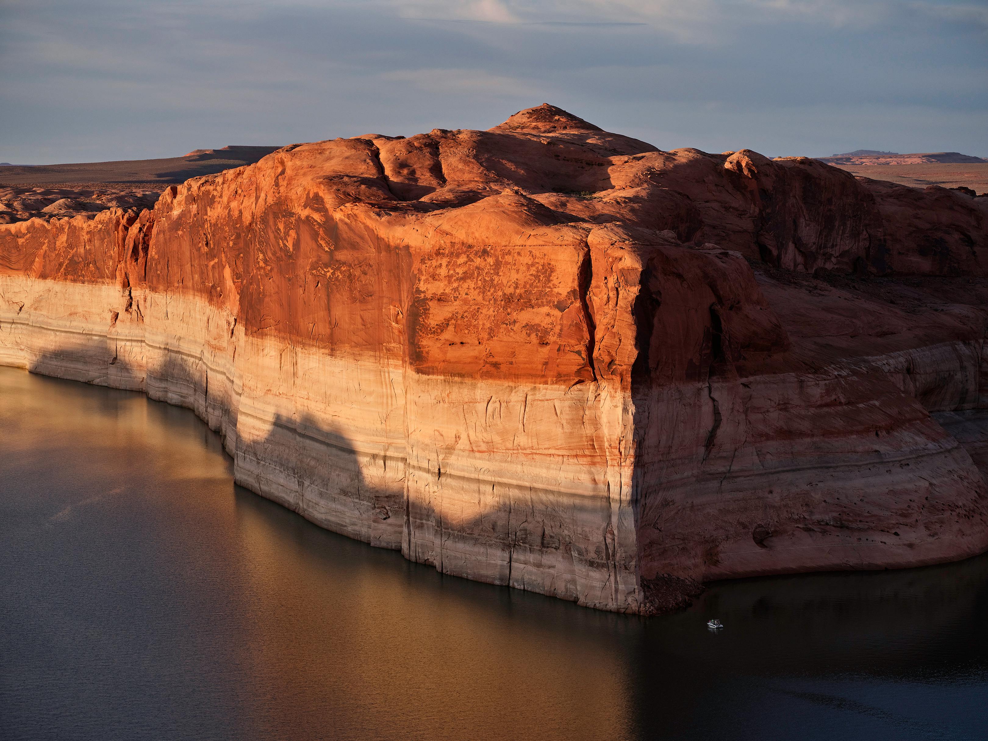 A photograph of Lake Powell showing extreme water loss in the cliffs and with a small boat for scale 