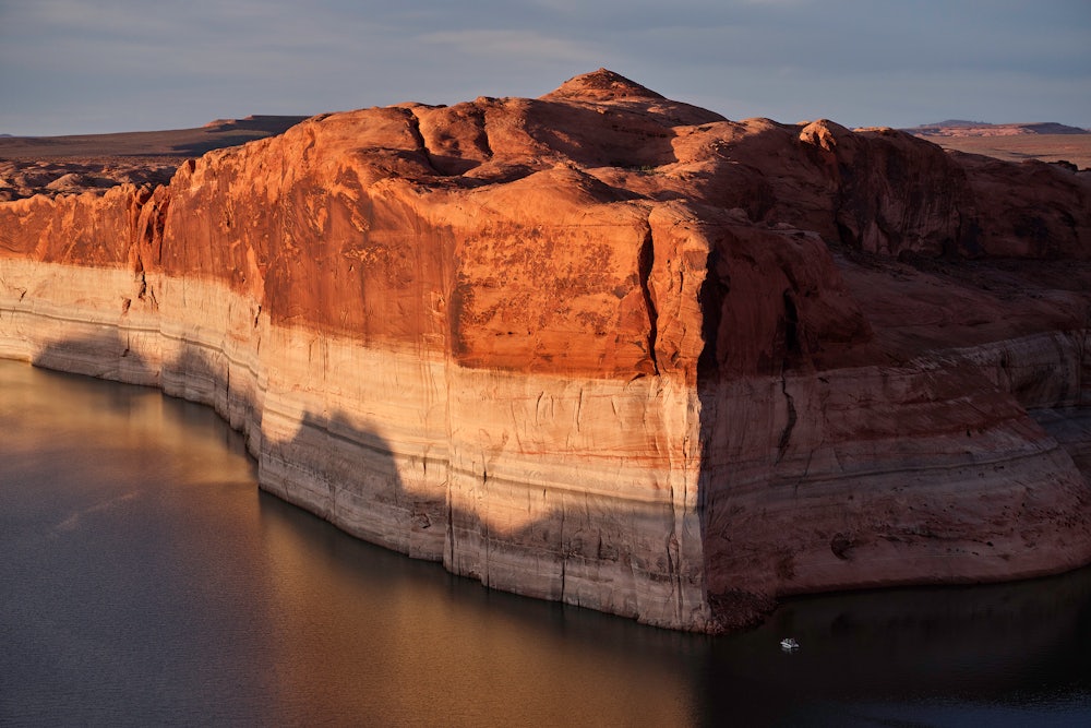 A photograph of Lake Powell showing extreme water loss in the cliffs and with a small boat for scale