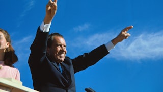 Richard Nixon extends both arms in a victory salute.