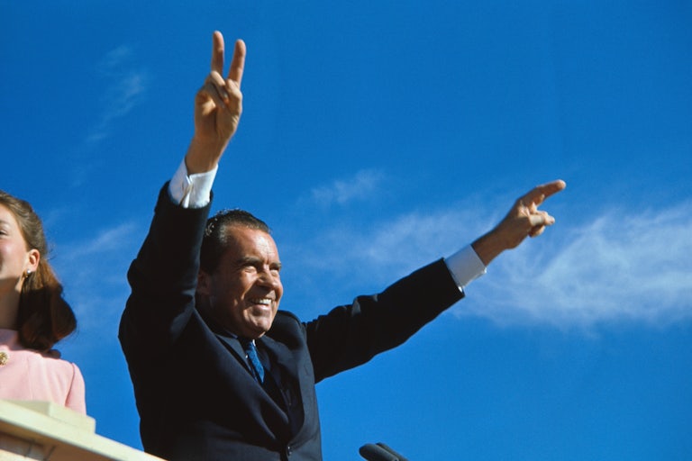 Richard Nixon extends both arms in a victory salute.