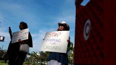 Two demonstrators stand next to a Target shopping cart holding anti-LGBTQ signs.