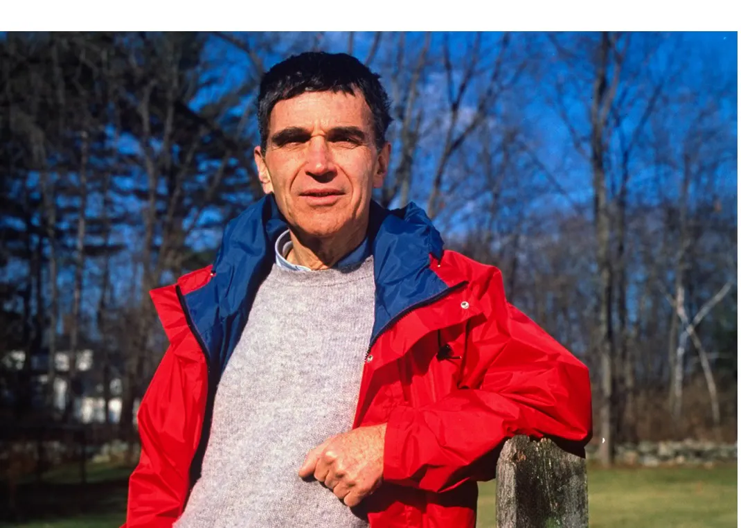 Harvard child psychologist Robert Coles standing outside, leaning against a wooden fence. 