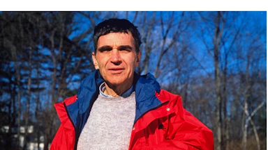 Harvard child psychologist Robert Coles standing outside, leaning against a wooden fence.