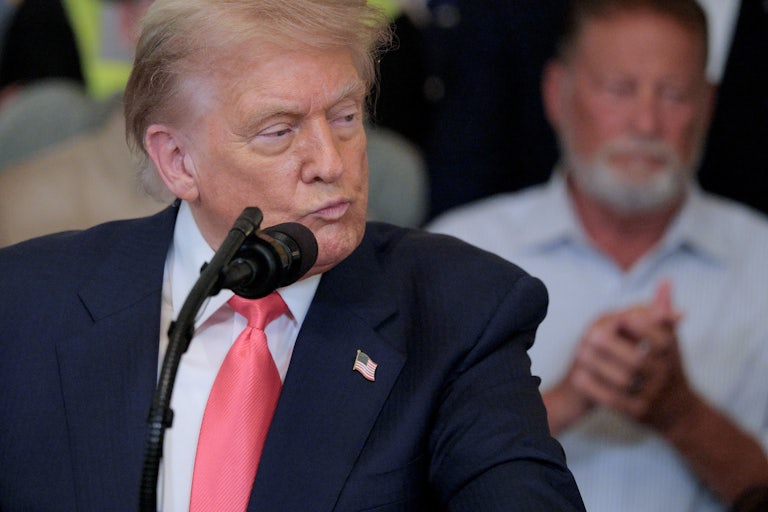 Donald Trump purses his lips while standing at a microphone