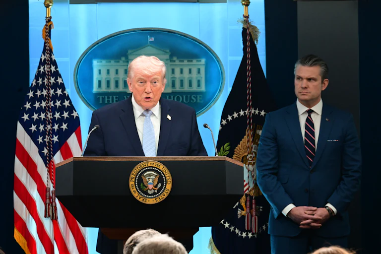 Donald Trump speaks at a podium. Defense Secretary Pete Hegseth stands next to him.