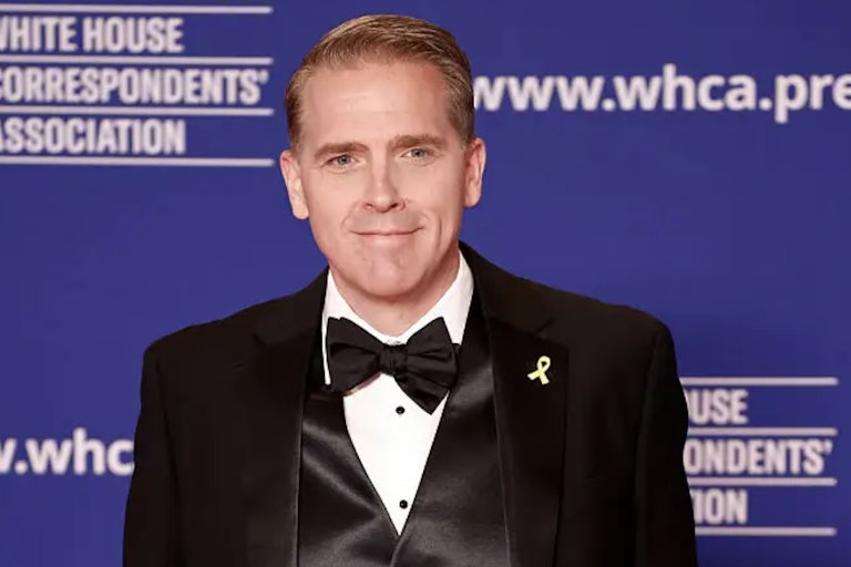 Scoot Jennings stands in front of a step and repeat at a WHCA event