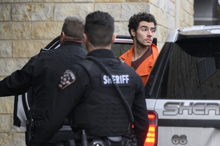 Luigi Mangione in an orange jumpsuit is led out of a car by several police officers
