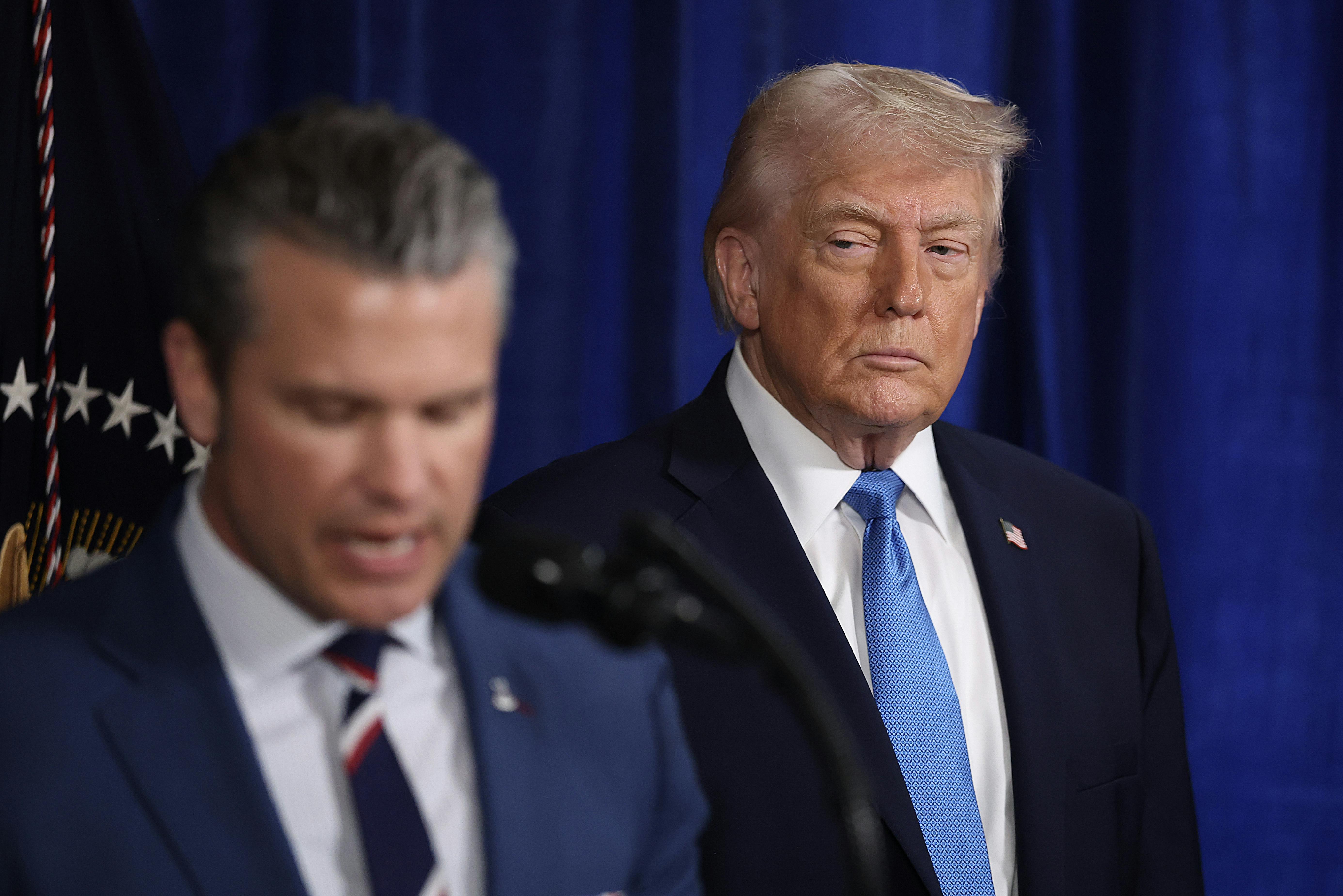 Donald Trump watches while Defense Secretary Pete Hegseth speaks at a podium