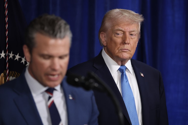 Donald Trump watches while Defense Secretary Pete Hegseth speaks at a podium