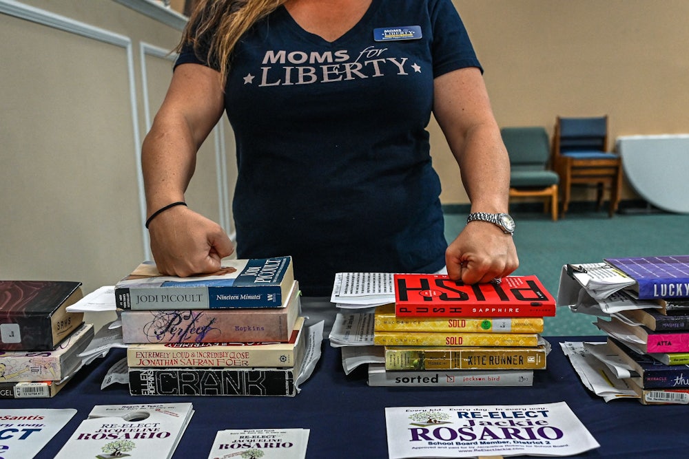 A woman rests her hands on stacks of books.