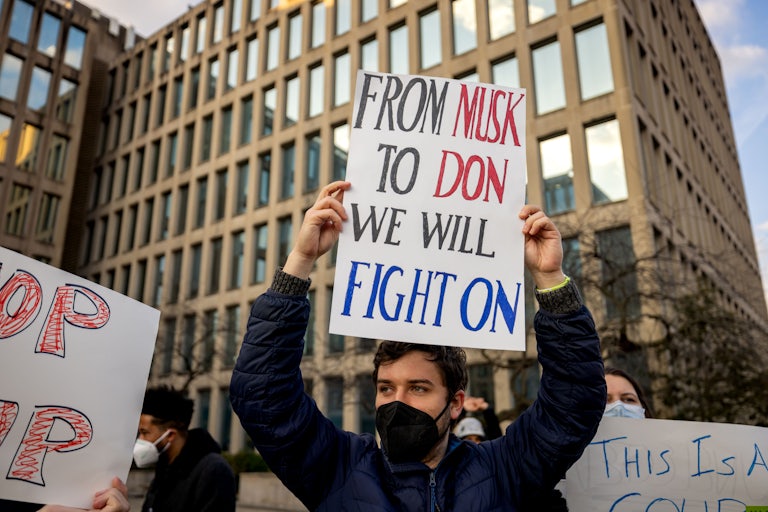 People hold up signs protesting against Elon Musk’s role in the government outside the OPM building in Washington, D.C.