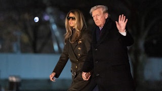 Donald and Melania Trump walk on the White House lawn hand in hand. Trump raises a hand for the camera.