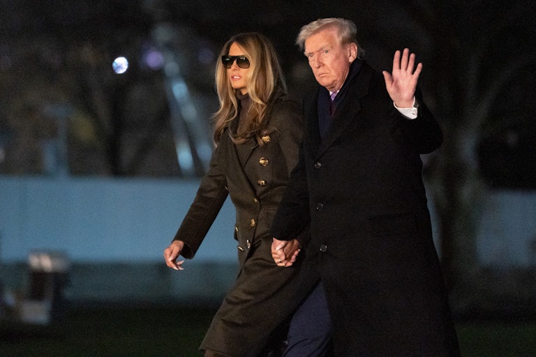 Donald and Melania Trump walk on the White House lawn hand in hand. Trump raises a hand for the camera.
