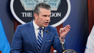 Defense Secretary Pete Hegseth points while standing at the podium