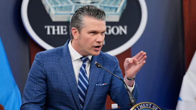 Defense Secretary Pete Hegseth points while standing at the podium