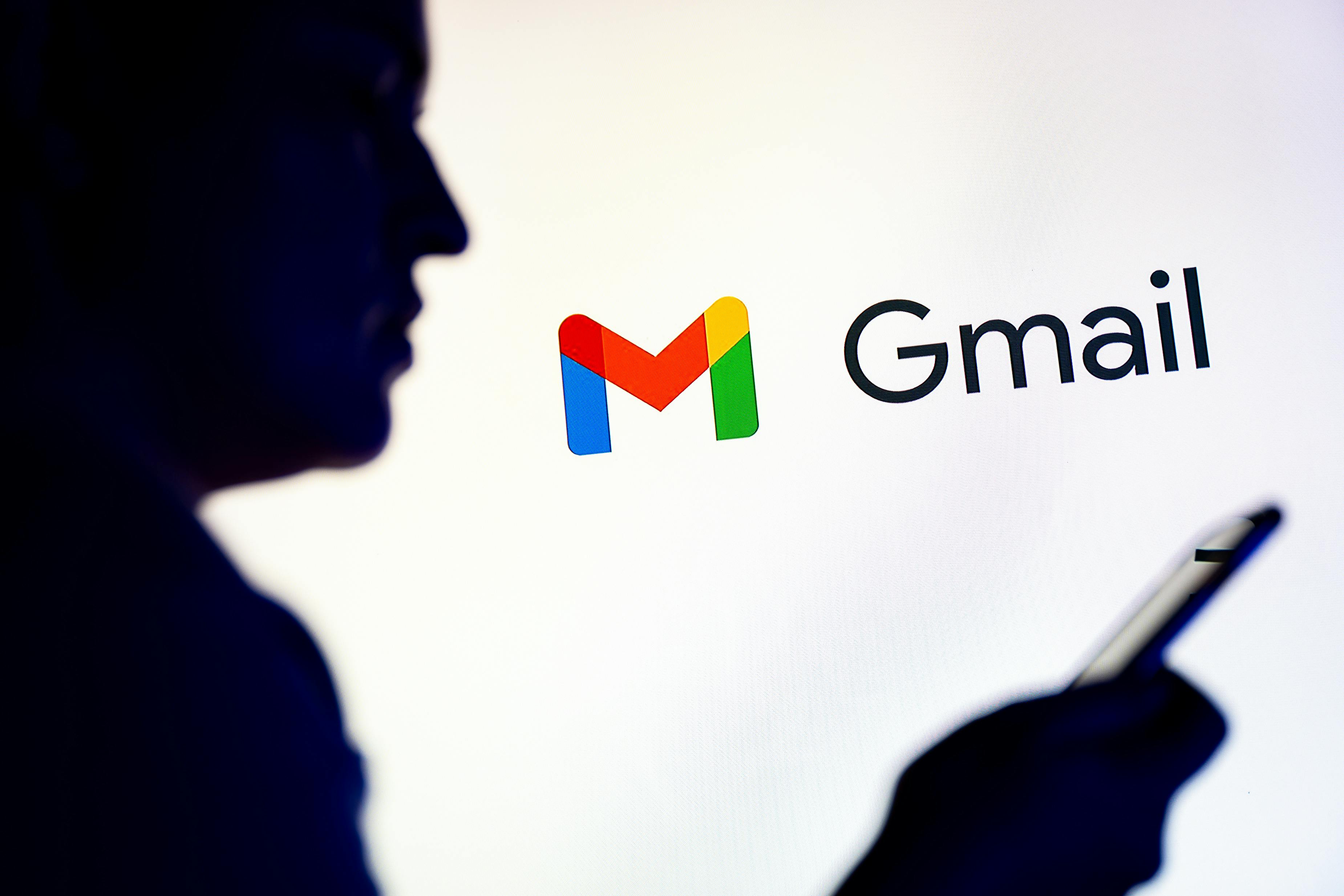 Silhoutte of a man looking at his phone while in front of the Gmail logo.