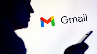 Silhoutte of a man looking at his phone while in front of the Gmail logo.
