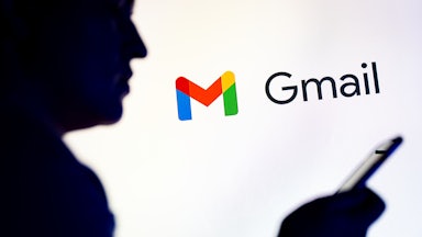 Silhoutte of a man looking at his phone while in front of the Gmail logo.