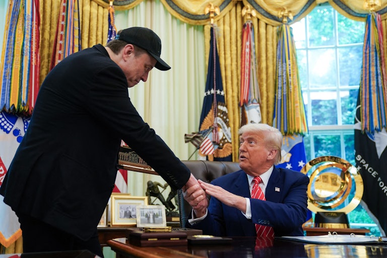 Elon Musk bows to Donald Trump as the two shake hands in the Oval Office of the White House, with Trump seated behind his desk.