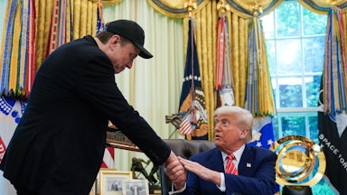 Elon Musk bows to Donald Trump as the two shake hands in the Oval Office of the White House, with Trump seated behind his desk.