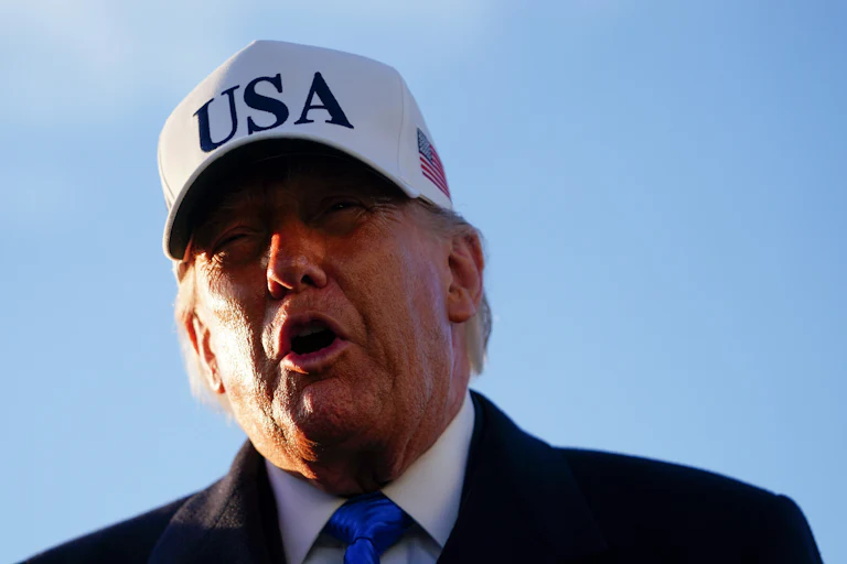 Donald Trump speaks while wearing a white cap that says "USA"