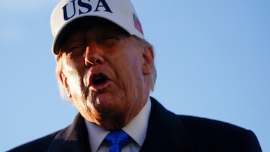 Donald Trump speaks while wearing a white cap that says "USA"