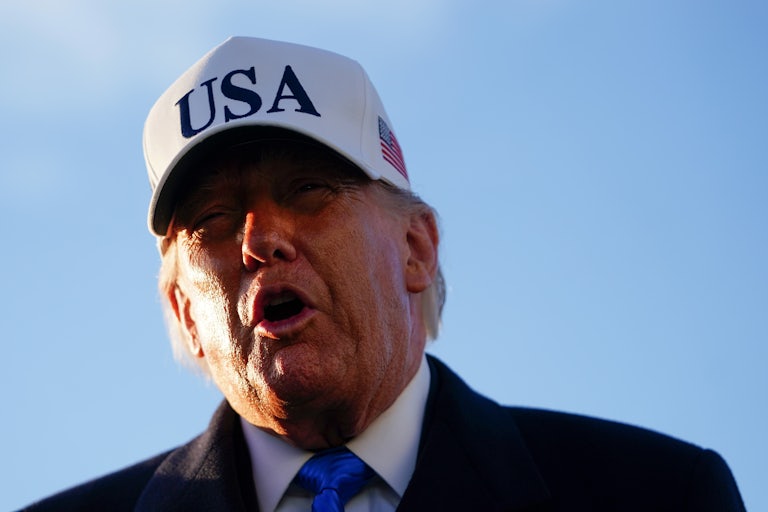 Donald Trump speaks while wearing a white cap that says "USA"