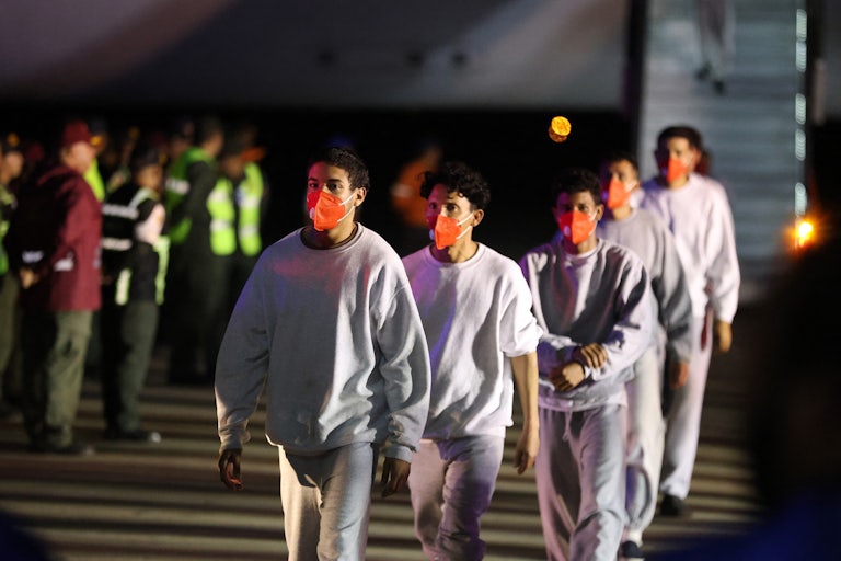 A group of 5 Venezuelan migrant men deported from Guantanamo Bay walk down from the Venezuelan Conviasa Airlines plane as they arrive at Simon Bolivar International Airport in Maiquetia, Venezuela. They wear gray sweatshirts and sweatpants and orange face masks.