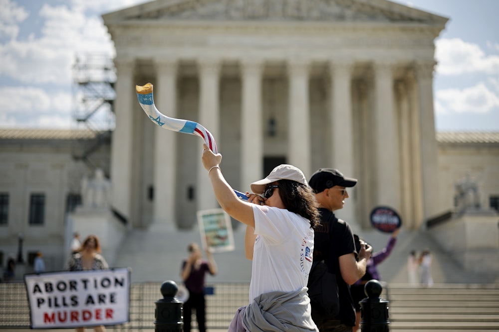 Demonstrators blow a shofar and hold a sign saying "abortion pills are murder."