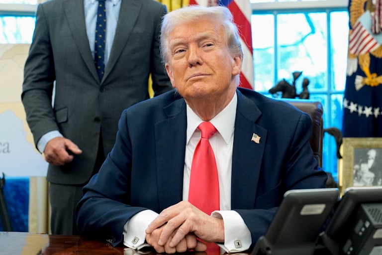 Donald Trump smiles while seated at his desk in the Oval Office