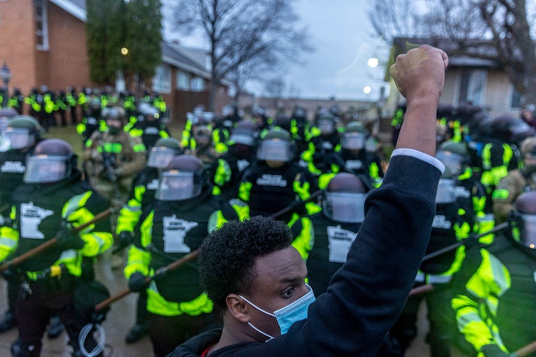 A man raises his fist as he faces the Minnesota State Troopers standing guard outside the Brooklyn Center Police Station