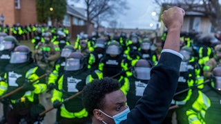 A man raises his fist as he faces the Minnesota State Troopers standing guard outside the Brooklyn Center Police Station